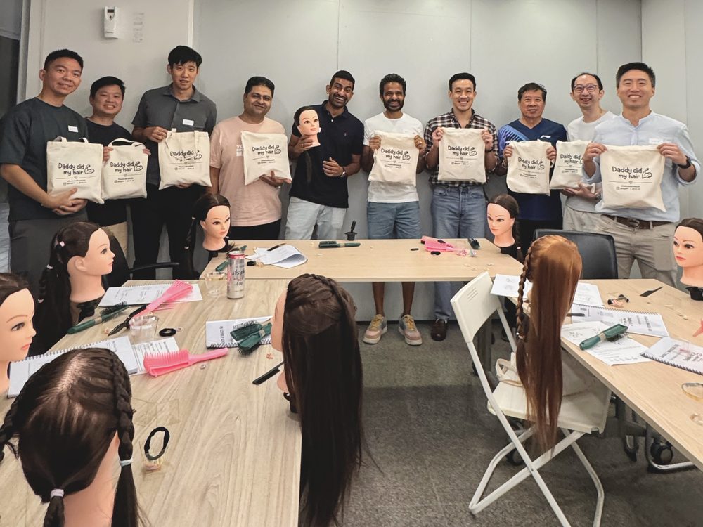 A group of dads holding up their Daddy did my hair tote bags after the workshop